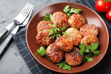 Delicious patties with parsley in bowl on grey textured table, closeup