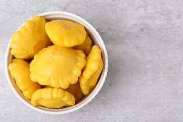 Pickled pattypan squashes in bowl on light grey table, top view. Space for text