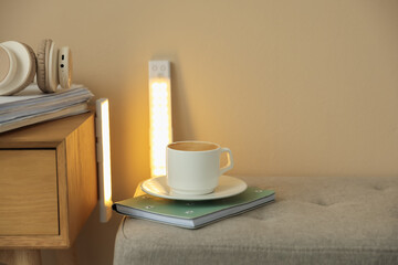 Coffee, notebook on pouf and portable LED lamps at home. Space for text