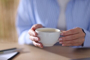 Woman having coffee break at table indoors, closeup