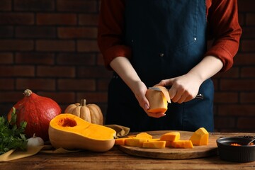 Woman peeling pumpkin at wooden table against brick wall, closeup