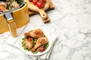 Grilled chicken drumsticks and air fryer basket with meal on white marble table, above view. Space for text
