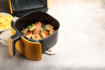 Air fryer basket with grilled chicken drumsticks, spices, green peas and french fries on grey table, closeup. Space for text
