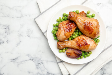 Grilled chicken drumsticks, green peas and onion on white marble table, top view. Space for text