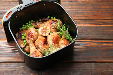 Air fryer basket with grilled chicken drumsticks, spices and green peas on wooden table, above view. Space for text