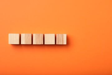 Wooden cubes on orange background, top view
