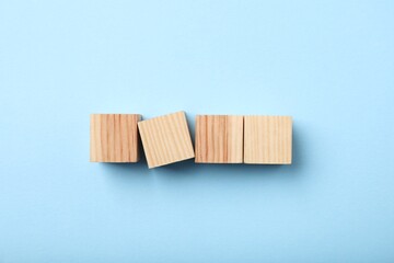 Wooden cubes on light blue background, top view