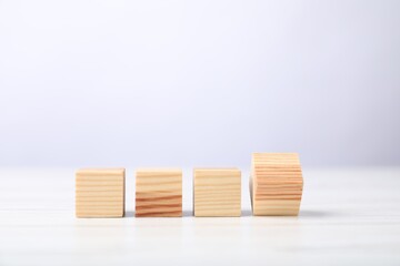 Blank cubes on white wooden table against light background, space for text