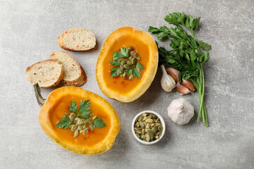Tasty pumpkin cream soup with seeds, parsley, garlic and bread on grey textured table, flat lay