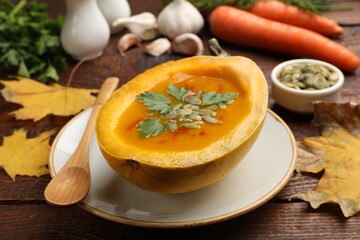 Tasty pumpkin cream soup with seeds and parsley among autumn leaves on wooden table, closeup