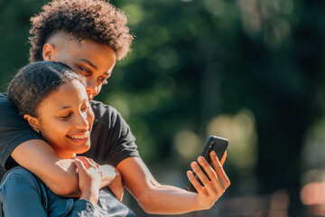 young romantic latin or hispanic couple outdoors embracing, looking at their cell phone or...