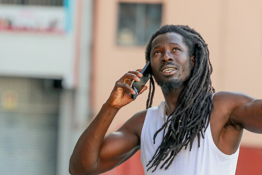 young man with afro hair or dreadlocks talking on mobile phone on the street