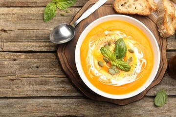 Delicious pumpkin cream soup with basil and seeds served on wooden table, flat lay