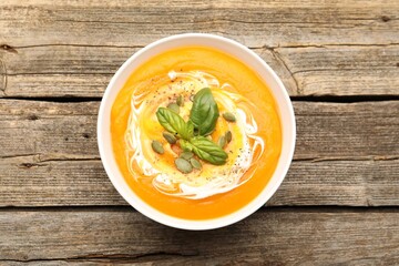 Delicious pumpkin cream soup with basil and seeds served on wooden table, top view
