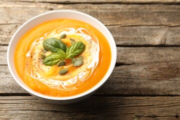Delicious pumpkin cream soup with basil and seeds served on wooden table, closeup. Space for text