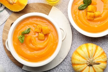 Delicious pumpkin cream soup with basil served on grey table, flat lay