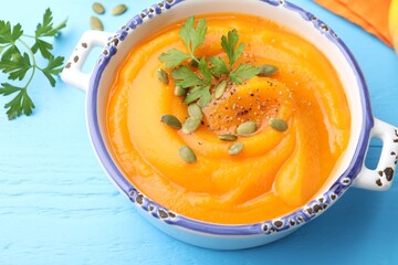 Delicious pumpkin cream soup with parsley and seeds served on blue wooden table, closeup
