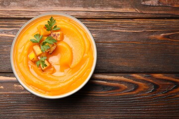 Delicious pumpkin cream soup with parsley served on wooden table, top view. Space for text