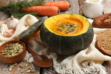 Tasty pumpkin cream soup with seeds and thyme served in pumpkin on table, closeup