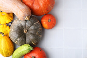 Many fresh pumpkins and other vegetables of gourd family on light tiled table, flat lay. Space for text