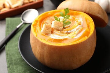 Tasty pumpkin cream soup with croutons and parsley served in pumpkin on grey table, closeup
