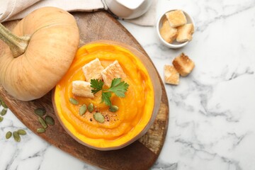 Tasty pumpkin cream soup with seeds, parsley and croutons served in pumpkin on white marble table, flat lay