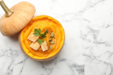 Tasty pumpkin cream soup with seeds, parsley and croutons served in pumpkin on white marble table, top view. Space for text