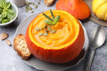 Tasty pumpkin cream soup with seeds and basil served in pumpkin on grey table, closeup