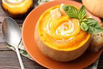 Tasty pumpkin cream soup with basil and croutons served in pumpkin on wooden table, closeup