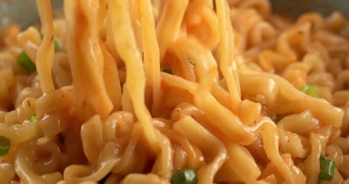 Korean spicy ramyeon noodle soup, with spices and green onions. Chopsticks pick up noodles.