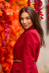 Portrait of a young woman with leaves in an autumn park. A stylish girl in a burgundy jacket strolls outdoors. Autumn fashion.