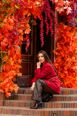 Portrait of a young woman with leaves in an autumn park. A stylish girl in a burgundy jacket strolls outdoors. Autumn fashion.