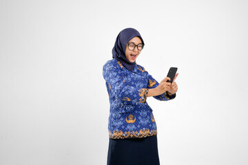 Smiling Indonesian civil servant woman in blue batik uniform using smartphone and feeling excited,...