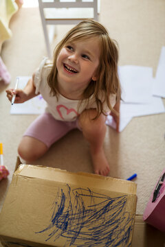 Child drawing on cardboard box and smiling indoors