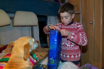 Boy unwrapping christmas gift with dog watching
