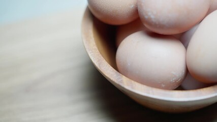 Slow motion macro top view of beige speckled eggs rotating counterclockwise in a wooden bowl on a table
