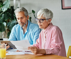 Senior couple checking bills and calculating expenses using a tablet at home, debt taxes and home...