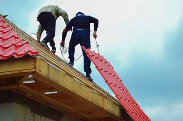 Two construction workers carry a sheet of metal roofing tiles to build a roof.
