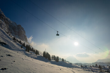 Aerial view of a lone gondola suspended between snowy peaks under a bright sun, casting long shadows across the alpine landscape, Davos, Graubunden, Switzerland.