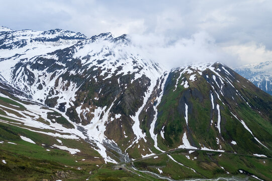 Aerial view of snow-capped peaks pierce the sky, their stark white contrasting sharply with the verdant slopes below, showcasing the majestic Furka Pass, Gletsch, Switzerland.