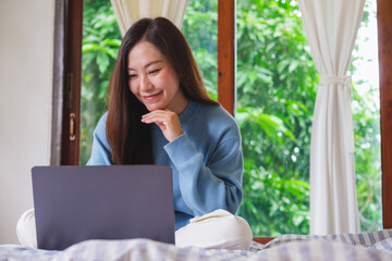 Portrait of a woman using and working on laptop computer while sitting on bed at home