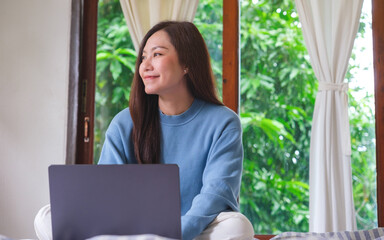 Portrait of a woman using and working on laptop computer while sitting on bed at home