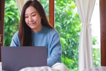 Portrait of a woman using and working on laptop computer while sitting on bed at home