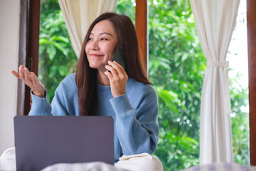 Portrait image of a beautiful woman talking on mobile phone while using laptop computer on the bed