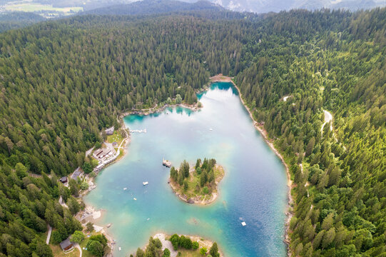 Aerial view of the serene, turquoise waters of Lake Cauma, nestled amidst a dense, emerald forest, Graubunden, Switzerland.