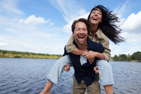 Couple enjoying playful piggyback ride by windy seaside outdoors