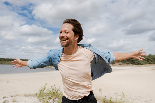 Smiling man with open arms enjoying wind in nature