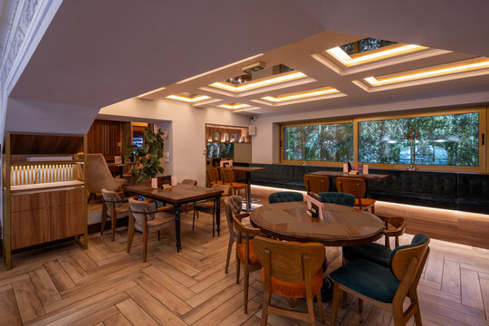 Modern café interior with wooden tables, colorful chairs, and warm ambient lighting and large windows