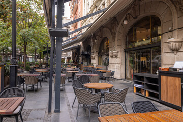 Outdoor café terrace with modern furniture, wooden tables, woven chairs, and large awnings
