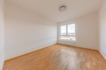 Bright and empty room with wooden flooring and large window boasting city views in the morning light